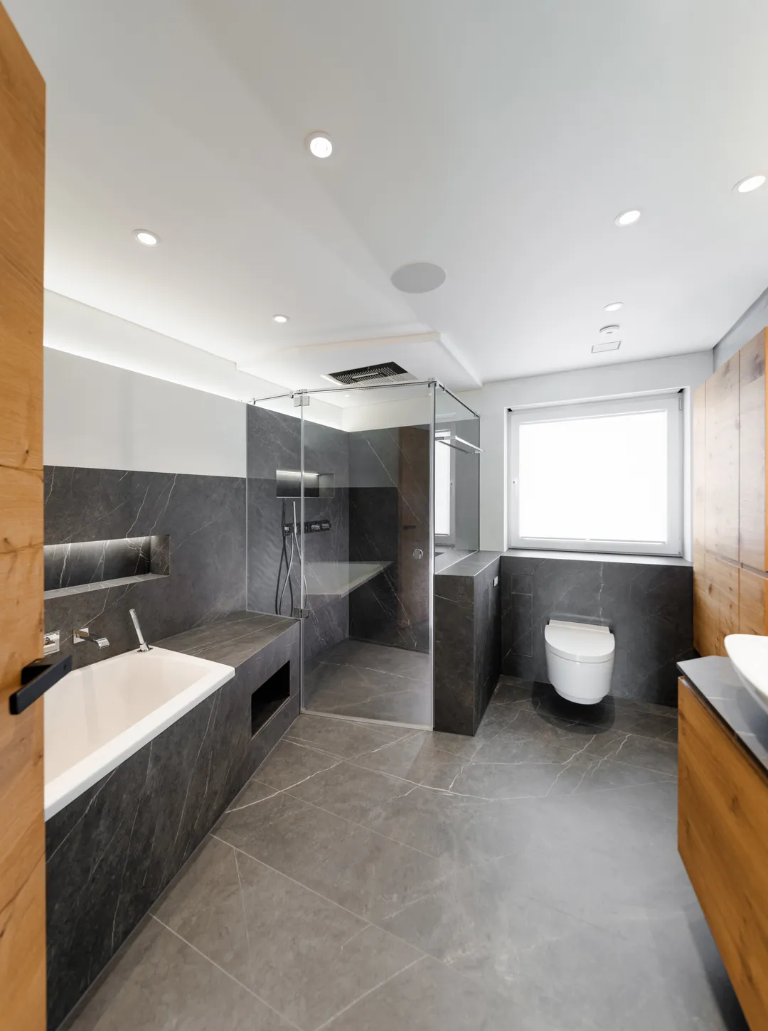 Barrierefreies Bad mit Fliesen in Anthrazit: Badewanne, bodengleiche Dusche hinter Glas und WC